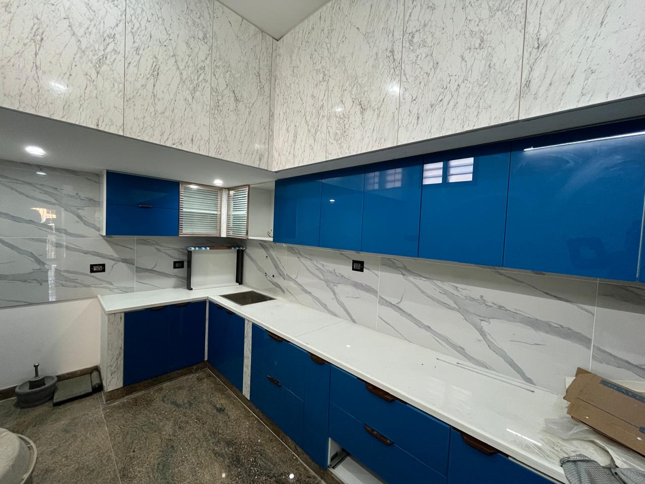 Modular kitchen with glossy blue cabinets and marble finish backsplash